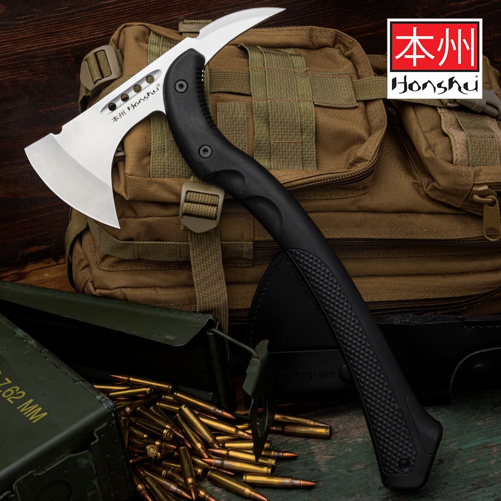 Curved tomahawk axe with a black nylon textured handle and stainless steel blade with Honsu printed in black on the center on a background of tactical gear. image number 0