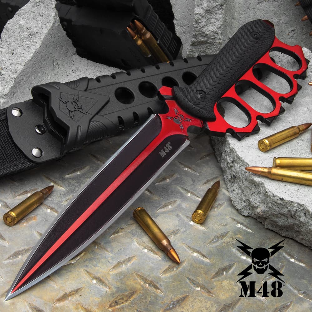 Double-edged trench knife with brass knuckle style handle with black oxide coating on a background of metal and concrete. image number 0