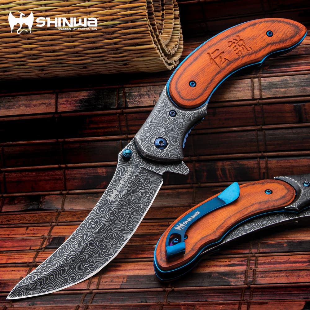 Shinigami bloodwood pocket knife with "raindrop patterned" blade and metallic blue accents on a background of orange toned bamboo. image number 0