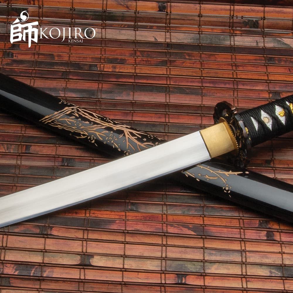 Kojiro sword 1045 carbon steel blade extends from hardwood grip lays crossed on top of black scabbard with hand carved marks image number 0