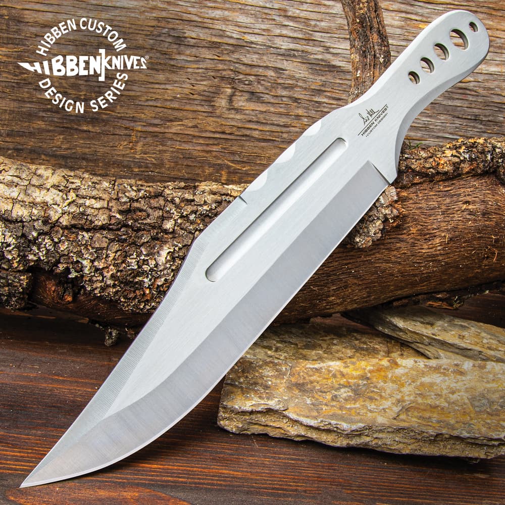 Polished stainless steel throwing knife with several thru-holes on a wood background. image number 0