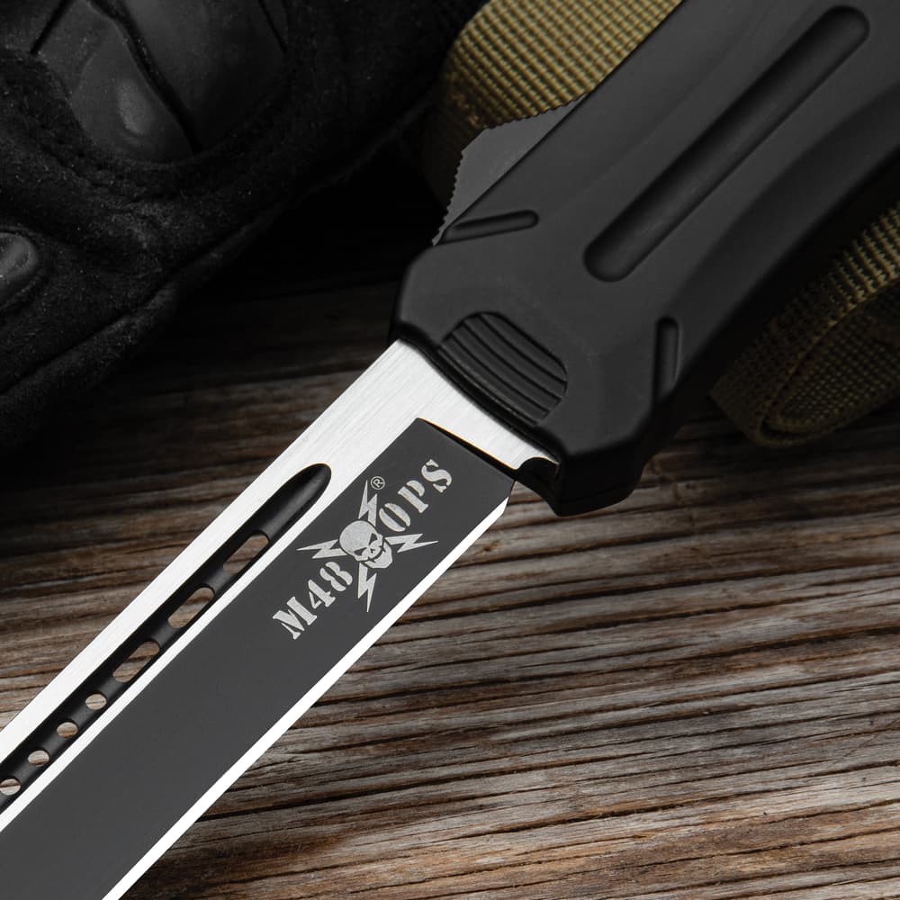 Closed OTF knife with a matte black handle and a pocket clip with a white "M48" logo inscription and a glass breaking pommel. image number 1