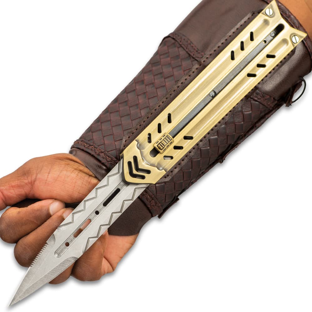 Silver blade with chevron engraving extended over palm of the hand while attached to gold sliding enclosure and mahogany braided faux leather arm sheath. image number 1