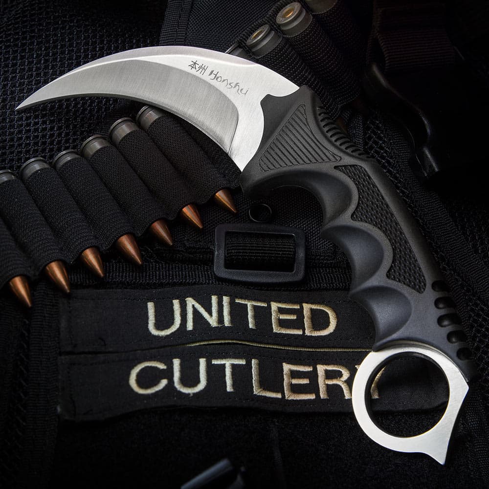 The 4” karambit with its textured handle and curved stainless steel blade is shown on a tactical background. image number 1