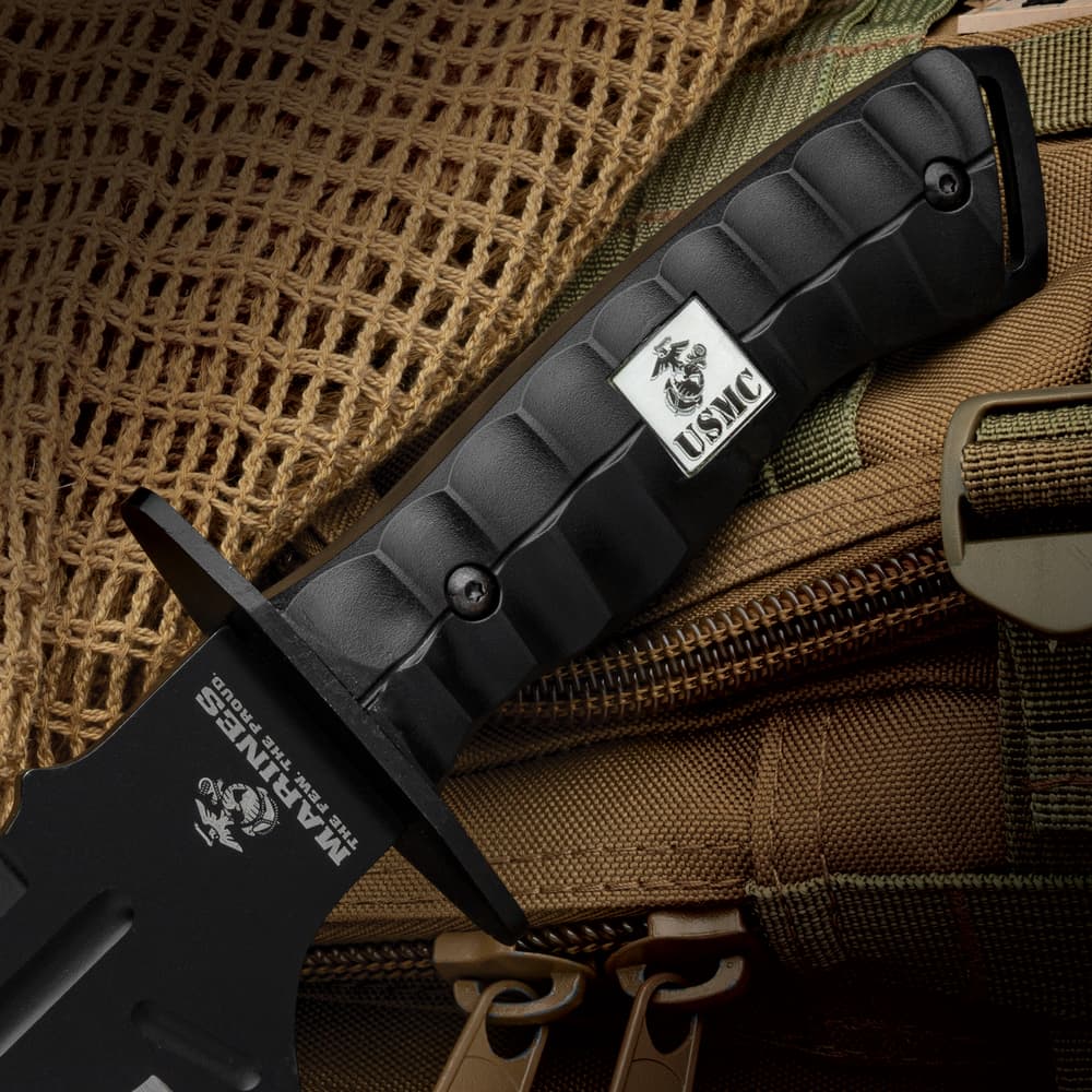 Zoomed view of the USMC Bulldog Bowie Knife black polypropylene handle with “USMC” logo, laid against a tactical backpack. image number 1