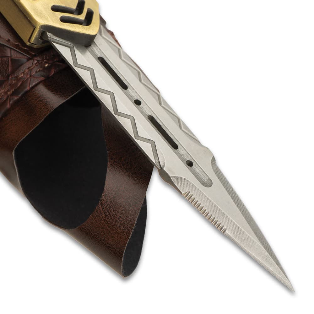 Upclose view of stainless steel blade with slight serations and chevron engravings with slight view of gold blade enclosure and mahogany faux leather. image number 2