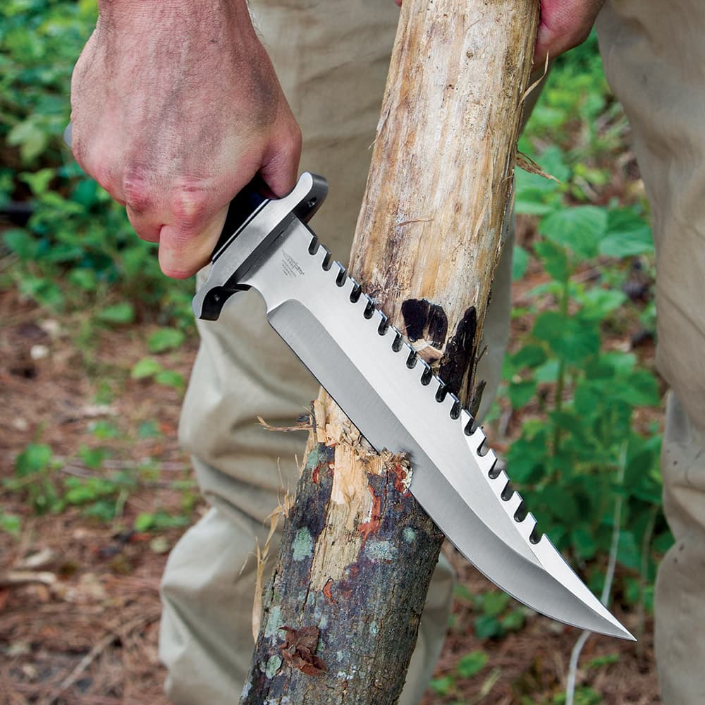The 15” knife has a 10” 7Cr17 stainless steel blade with sawback teeth, shown slicing into a tree. image number 2