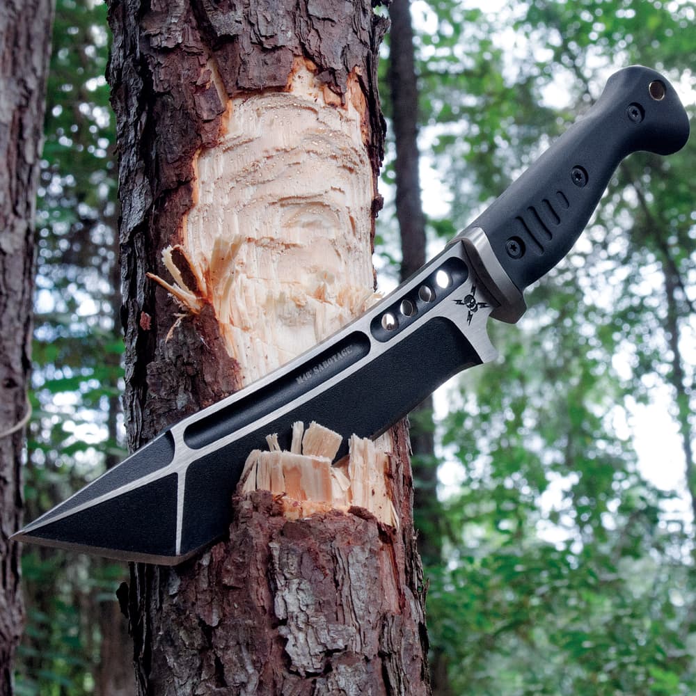 The knife’s black stainless steel blade is shown sliced into the side of a tree. image number 2