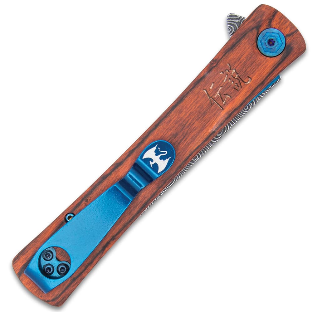 Closed pocket-knife with a bloodwood handle with japanese inscriptions and metallic blue accents including a pocket clip with a dragon carving on a white background. image number 2