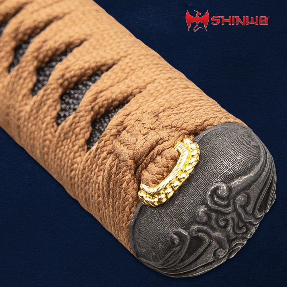 The pommel of the katana is shown with intricate wave-like design atop the brown cord wrapped handle. image number 2