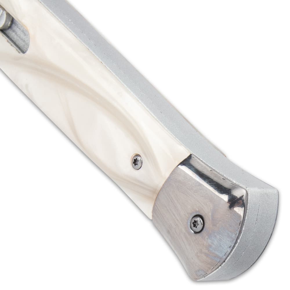 Upclose angled view of the end of a pearl handle switchblade with mirror polished silver accents. image number 3