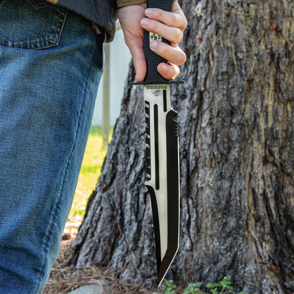 angled view of a "USMC" sawback knife with serations on both edges of the blade and a sturdy handguard. image number 3