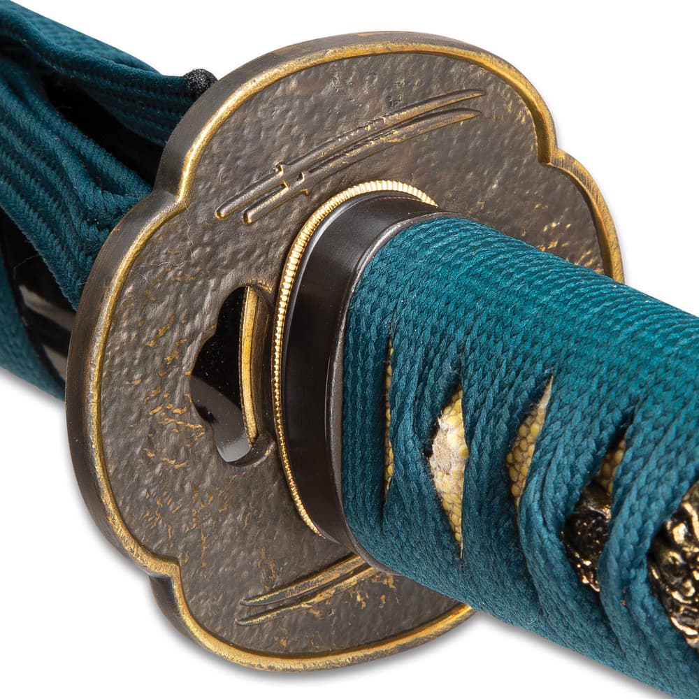 Zoomed view of brass tsuba embossed with double swords on each side showcasing tea dyed rayskin wrapped in a teal cord image number 3
