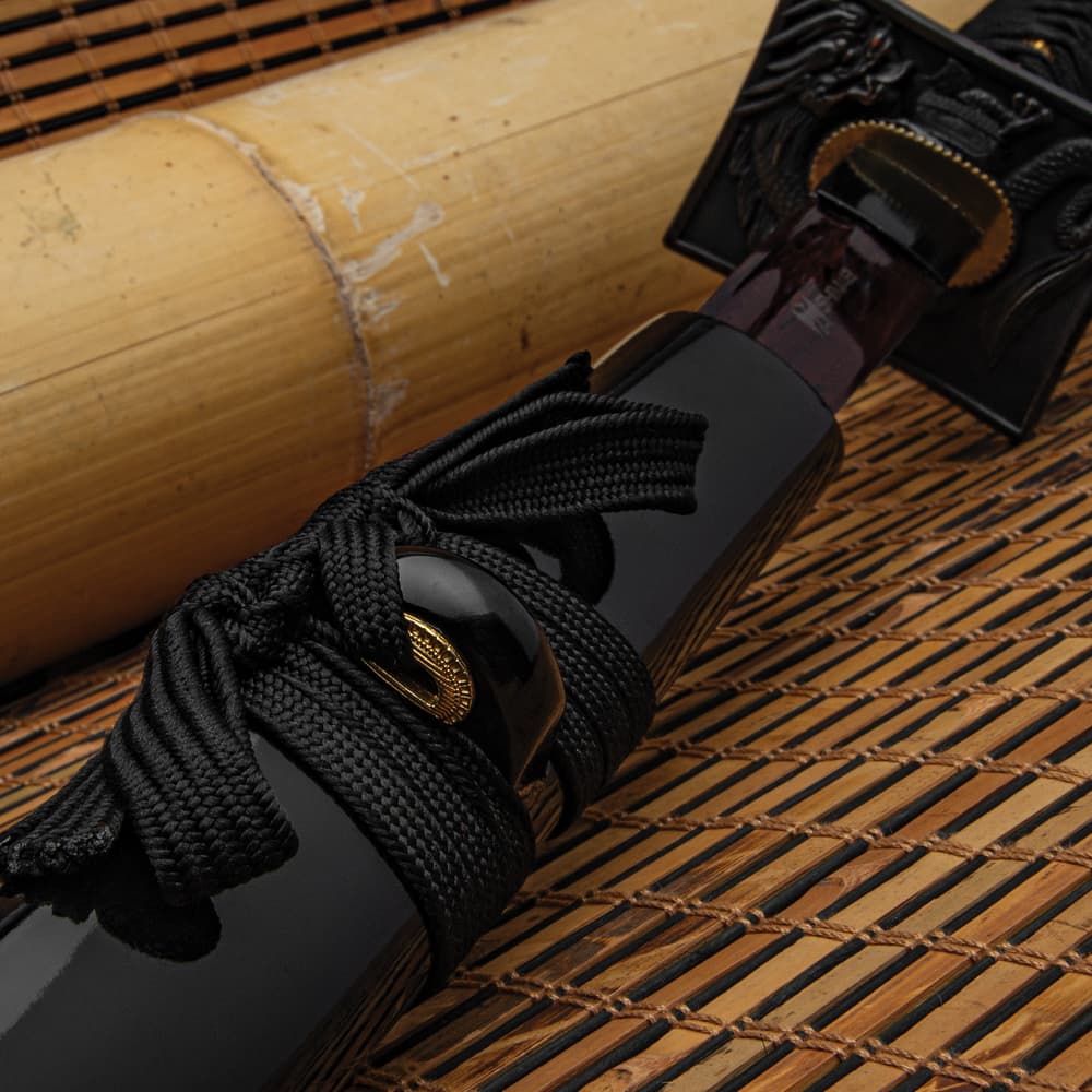 A close view of a black katana scabbard with a black and gold knob wrapped with a black cord image number 4