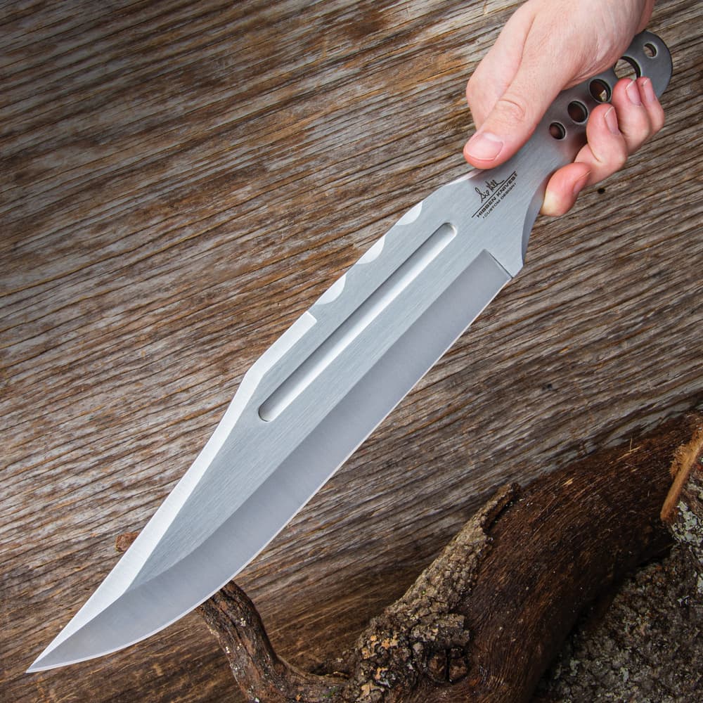 Large "Gil Hibben" mirror polished throwing knife being held diagonally in front of a wood background. image number 5