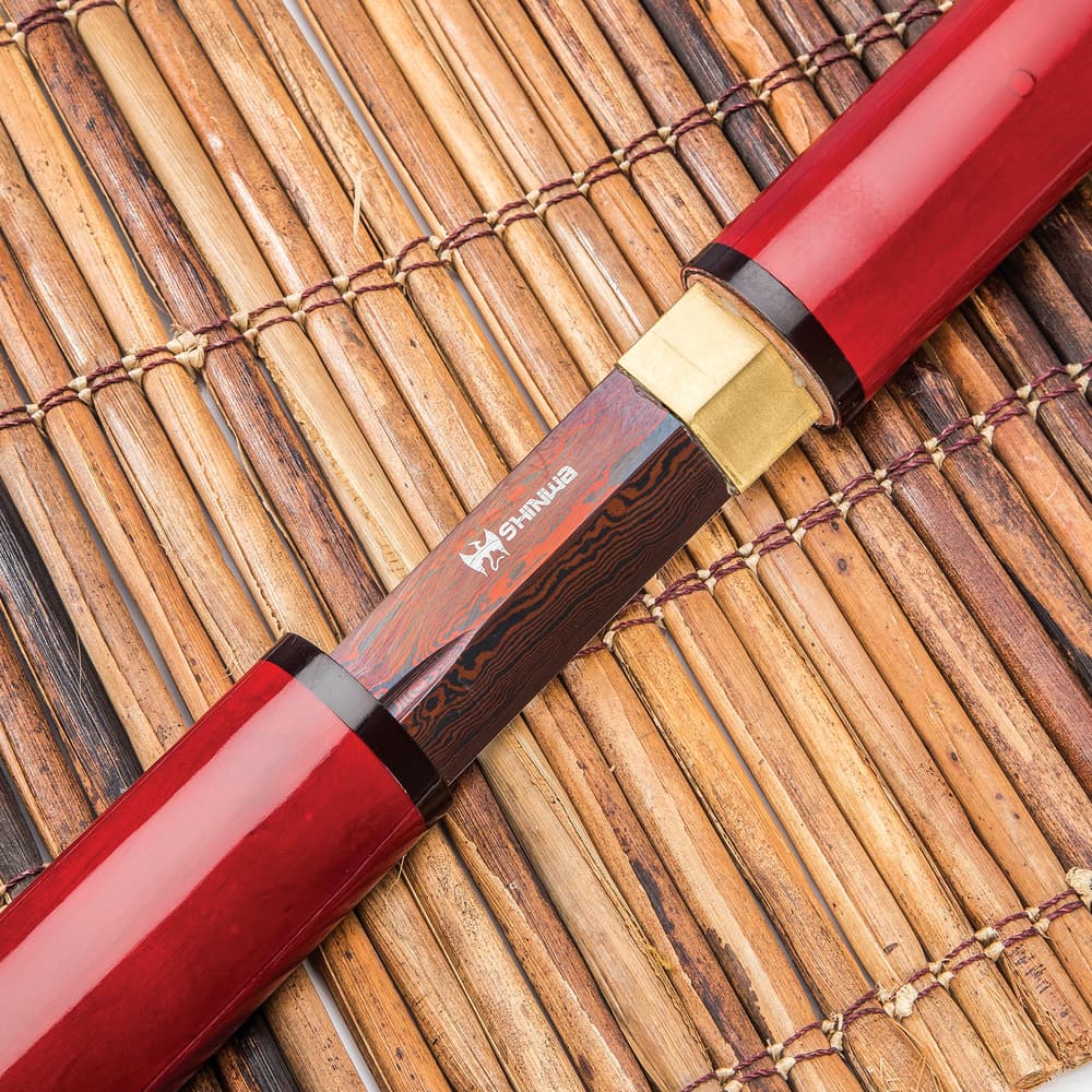 The black Damascus steel blade shown sliding into the red lacquered scabbard atop a bamboo mat. image number 7
