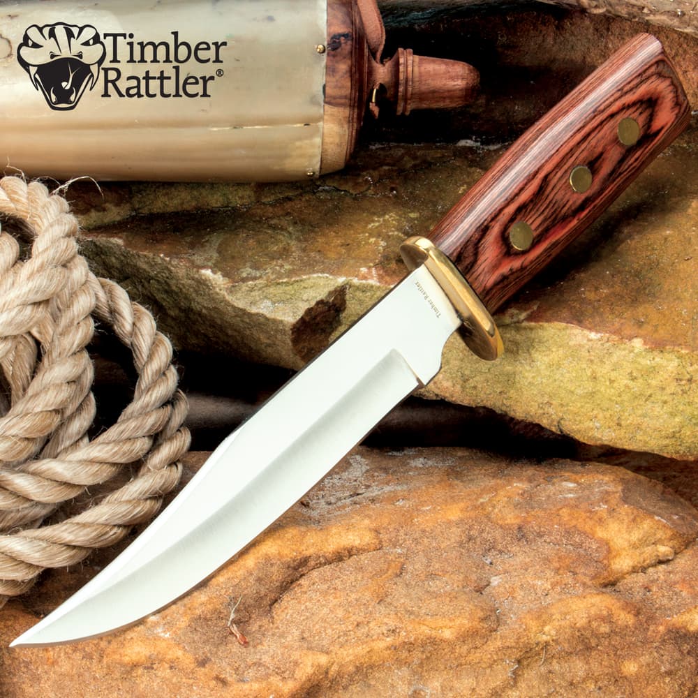 Bowie knife with wooden handle on rocks and rope image number 0