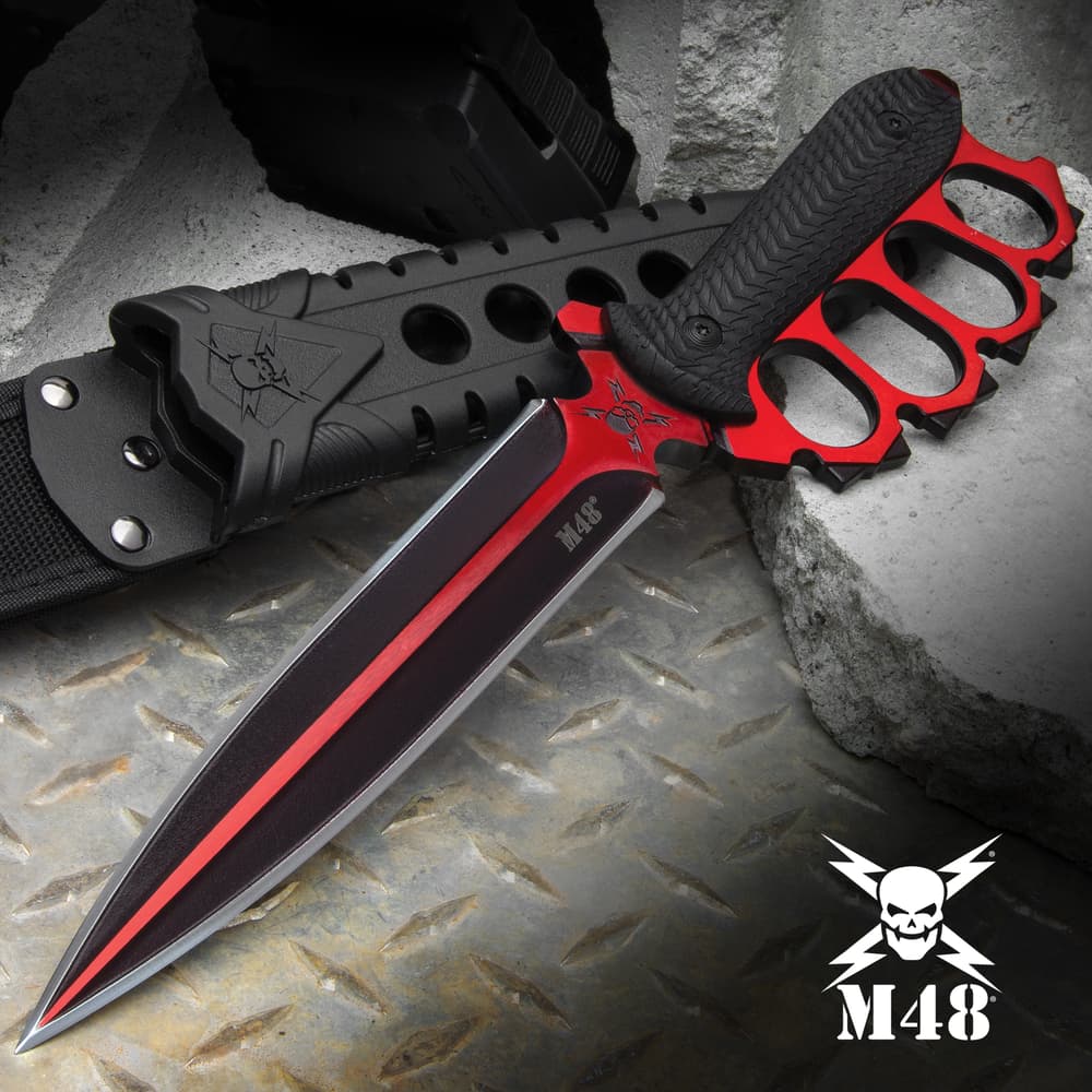 Double-edged trench knife with brass knuckle style handle with black oxide coating on a background of metal and concrete. image number 0