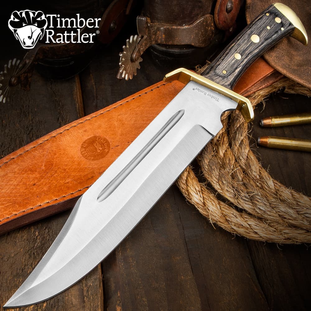 Large bowie knife with wooden handle and leather sheath on wooden surface image number 0