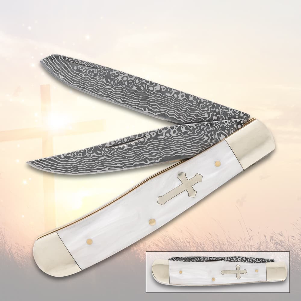 Folding knife with patterned blades and cross design on handle, set against a soft background image number 0