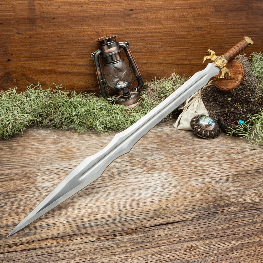 Sword with brass hilt on wooden surface, surrounded by moss and objects image number 0