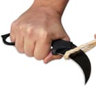 A hand is shown holding the karambit and using its curved black 7Cr13 stainless steel blade to cut a rope.