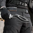 A gloved hand is shown holding the kukri by its TPR handle, showcasing the curved stainless steel black with thru holes.