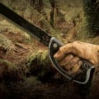 A muddy hand is shown holding the black rubberized injection molded handle of the machete.
