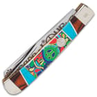 The handle is white bone with colorful, 3D-printed peace sign artwork, accented with wooden and teal blue panels