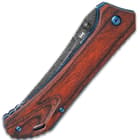 This knife has reddish-brown wooden handle scales, secured by metallic blue screws.