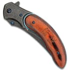 Closed bloodwood pocket knife with a raindrop patterned blade and metallic blue accents along with a japanese inscription in the wooden handle. 
