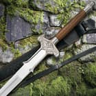 The Barbarian II sword is shown on top of its leather scabbard with focus on the brown hardwood handle and brass-plated accents. 