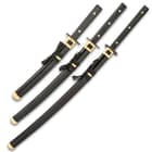 Three Samurai swords side by side with black scabbards and black handle, all with brass detailing. 