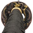 The hardwood handle is wrapped in faux rayskin and black cord and has an intricately detailed metal alloy tsuba