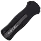 Closed black OTF pocket knife showing the satin grey pocket clip with an inscription of "The Infidel" upon it.
