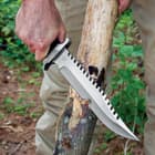 The 15” knife has a 10” 7Cr17 stainless steel blade with sawback teeth, shown slicing into a tree.