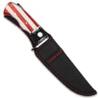 Large bowie knife with an American flag handle with “2nd Amendment” printed onto the flag enclosed in a black sheath with red stitching and “Timber Wolf” embroidered in the center. 