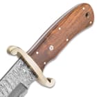 The brown wooden handle scales are secured to the tang by brass pins and the handle features intricate rosette accents and a lanyard hole