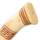 The rounded and uniquely curved handle is crafted of natural bone, accented with bands of brass filework and red spacers