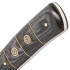 The handle scales are crafted of a dark wood, accented with brass rosettes and spacers and secured with brass pins