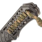 The tough, black ABS handle features camouflage paracord woven into it, extending into a short lanyard, and it has a glass breaker