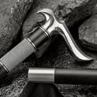 Zoomed view of the mirror polished handle and matching cane end on top of black rocks. 