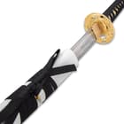 Close view of sword with shinwa etched on the inner side of blade extended to gold like hand guard peeking out of scabbard
