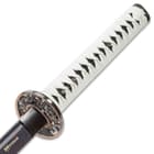 White braided cord wraps the faux rayskin handle of the sword with brass menuki. 