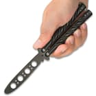 A hand is shown holding the 8 3/4” black butterfly trainer with unsharpened false edge blade with weight reducing thru holes.
