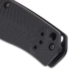 Upclose view of the lanyard opening on the end of the matte black G10 handle with a milled chevron pattern.
