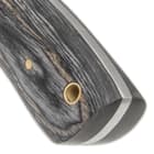 Attached to the tang with brass pins, the weathered gray pakkawood handle scales also feature a brass insert lanyard hole