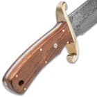 The brown wooden handle scales are secured to the tang by brass pins and the handle features intricate rosette accents and a lanyard hole