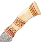 The rounded and uniquely curved handle is crafted of natural bone, accented with bands of brass filework and red spacers