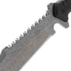 Upclose view of a M48 titanium electroplated blade with a partial sawback spine with jagged edges and a "M48" logo on the blade. 
